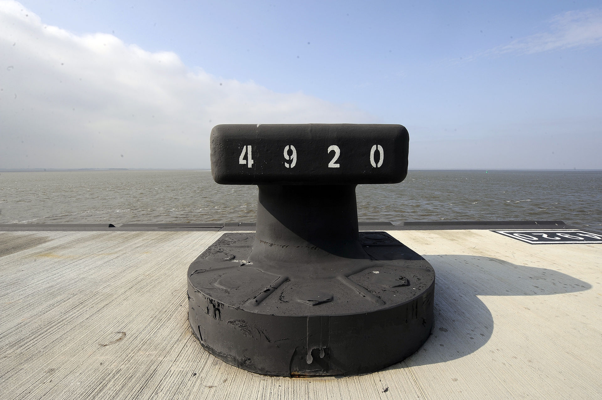 Ein schwarzer Poller mit weiße aufgepinselter Nummer 4920. Im Hintergrund Wasser/Weser